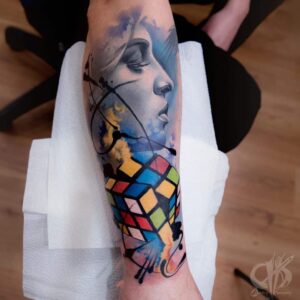 Surrealistische tattoo op onderarm, gezet bij Inksane tattoo en piercing. Vrouwengezicht met rubics cube.
