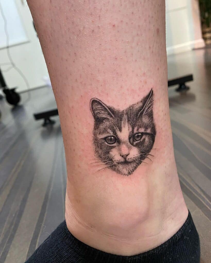 Black and grey tattoo van een klein kattenhoofdje in dotwork op de enkel