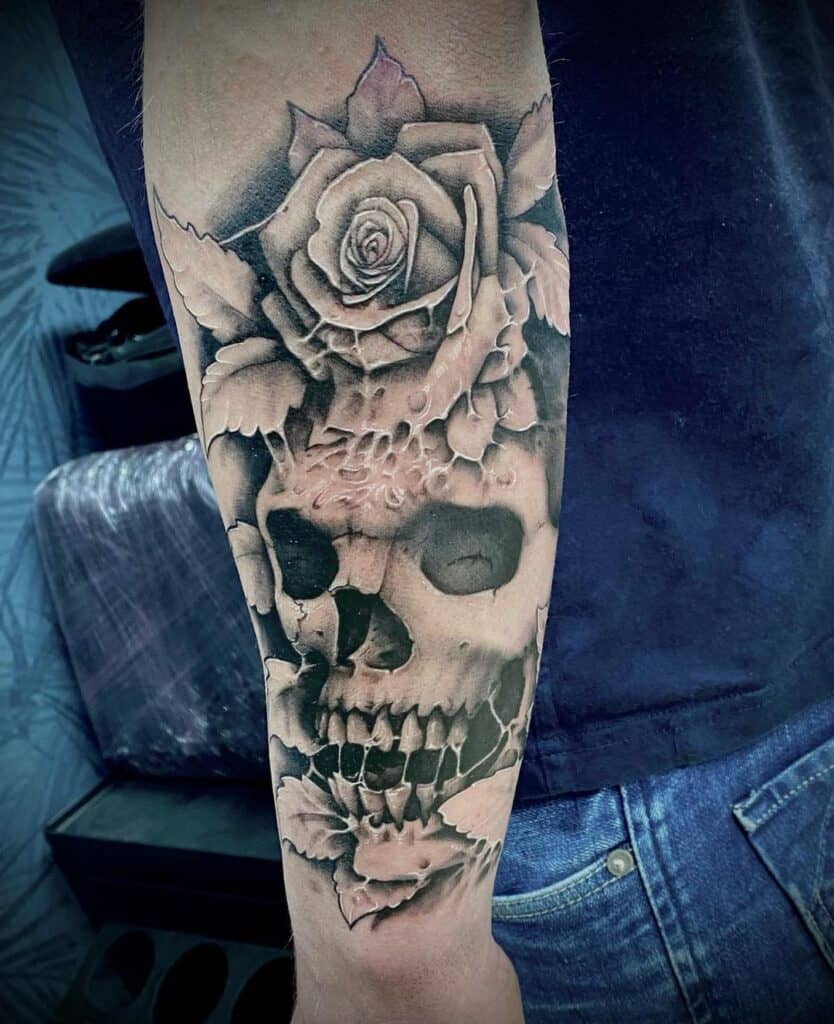 Black and grey realisme tattoo op de onderarm. Schedel met roos op het voorhoofd