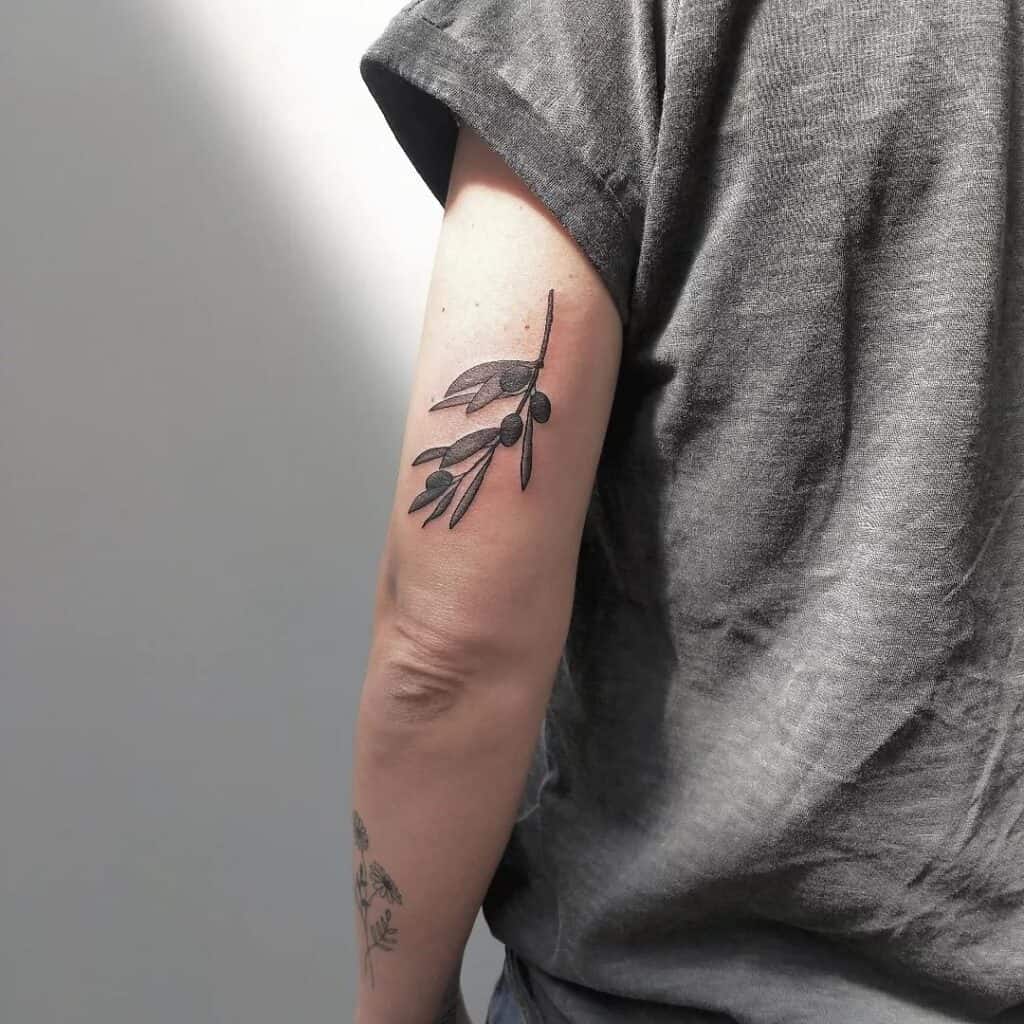 Black and grey tattoo op de achterkant van de bovenarm, takje met besjes en blaadjes