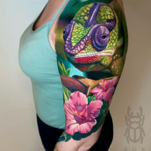 Kleur realisme tattoo op bovenarm gezet bij Inksane tattoo en piercing. Kameleon op een tak met bloemen.
