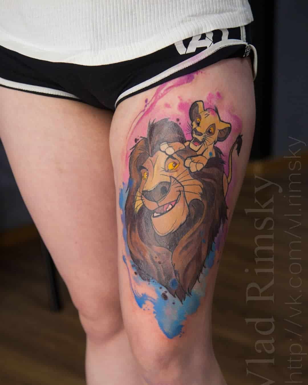 Kleurentattoo van Mufasa en Simba van The Lion king op het bovenbeen met watercolor achtergrond. Gezet bij Inksane tattoo en piercing.
