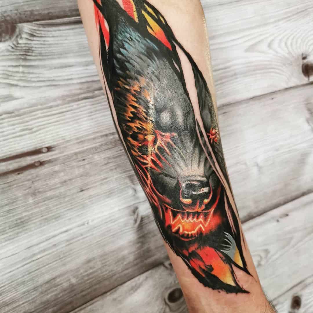 Tattoo van een demonische wolf op een onderarm. Zwarte wolf met rode en oranje kleuren om een gloeieffect te verkrijgen rond de ogen en de mond.