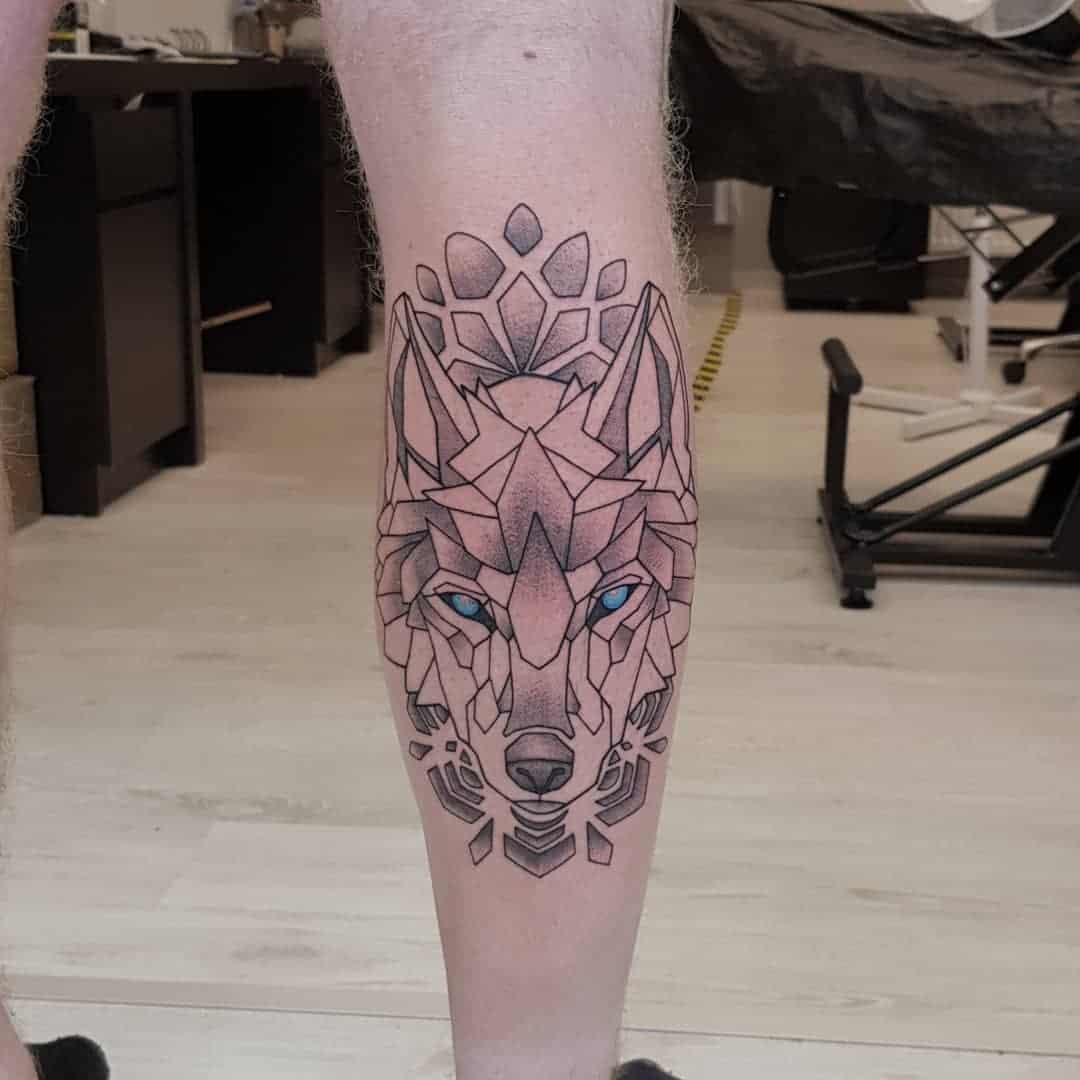 Geometrische tattoo van een wolf op een kuit. Black and grey met blauwe ogen.